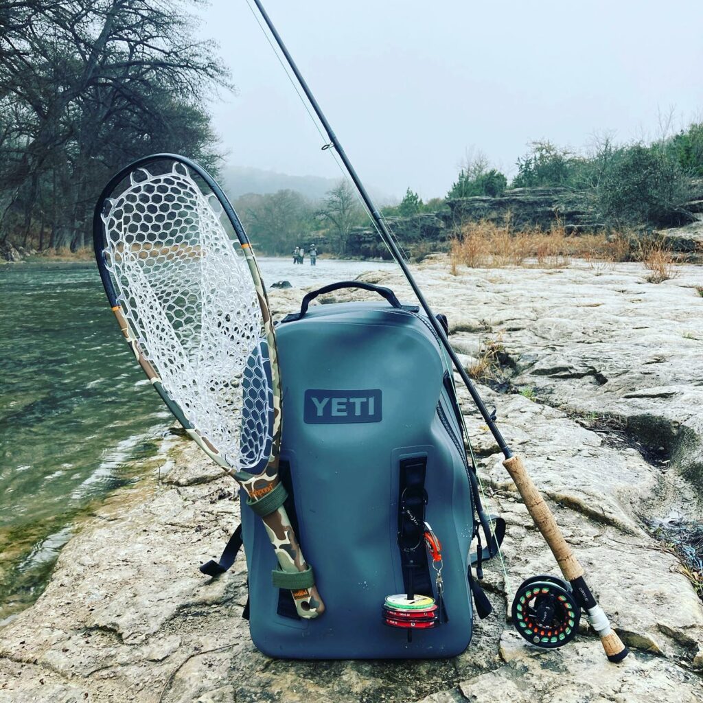 This photo from our best fly fishing backpack guide shows a Yeti backpack on a shore.
